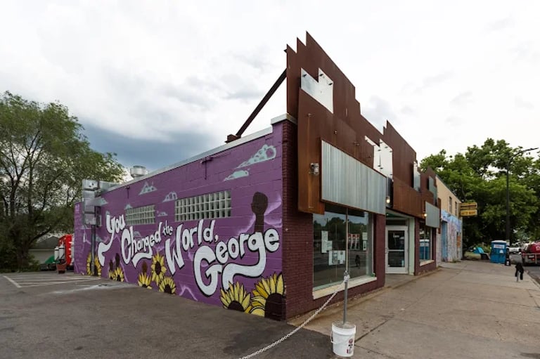 A purple mural on a brick building reads You Changed the World George in honor of George Floyd.
