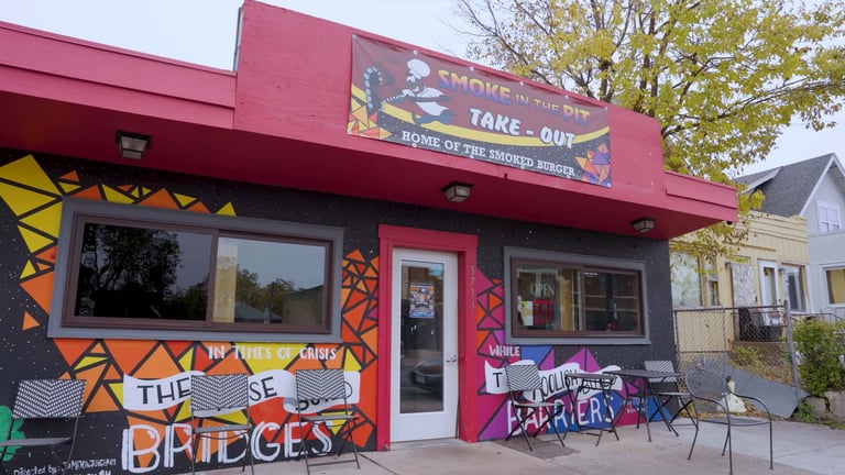 Smoke in the Pit take-out BBQ restaurant exterior with colorful mural art and outdoor seating.
