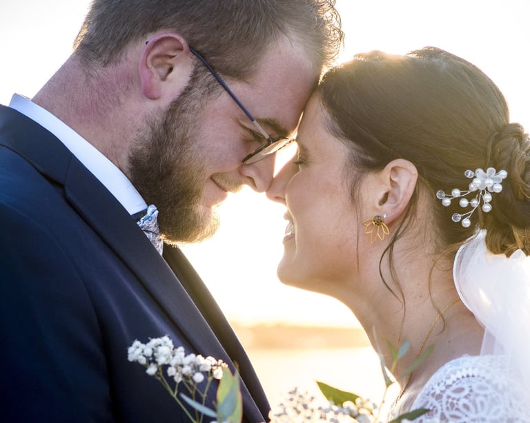 A happy bride and groom touching foreheads during a golden hour outdoor wedding photoshoot.