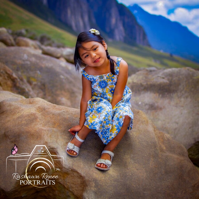 a little girl sitting on a rock in a mountain posing for portrait