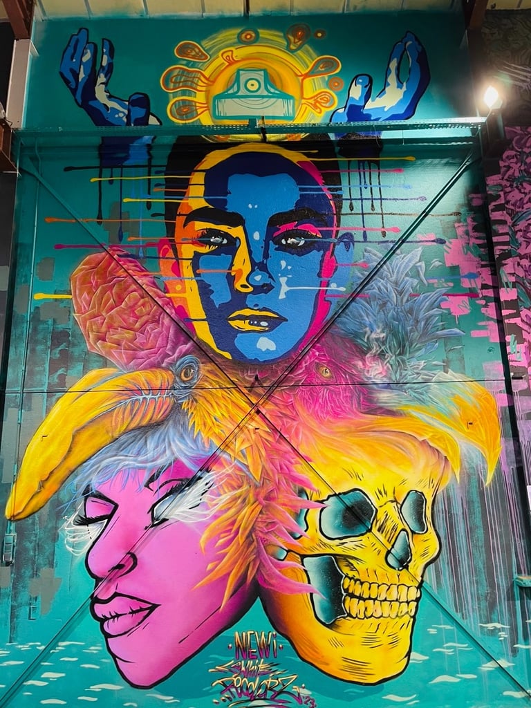 une fresque avec un crâne, une tête violette, deux tête d'oiseau colorés, deux mains et une tête colorée de façe