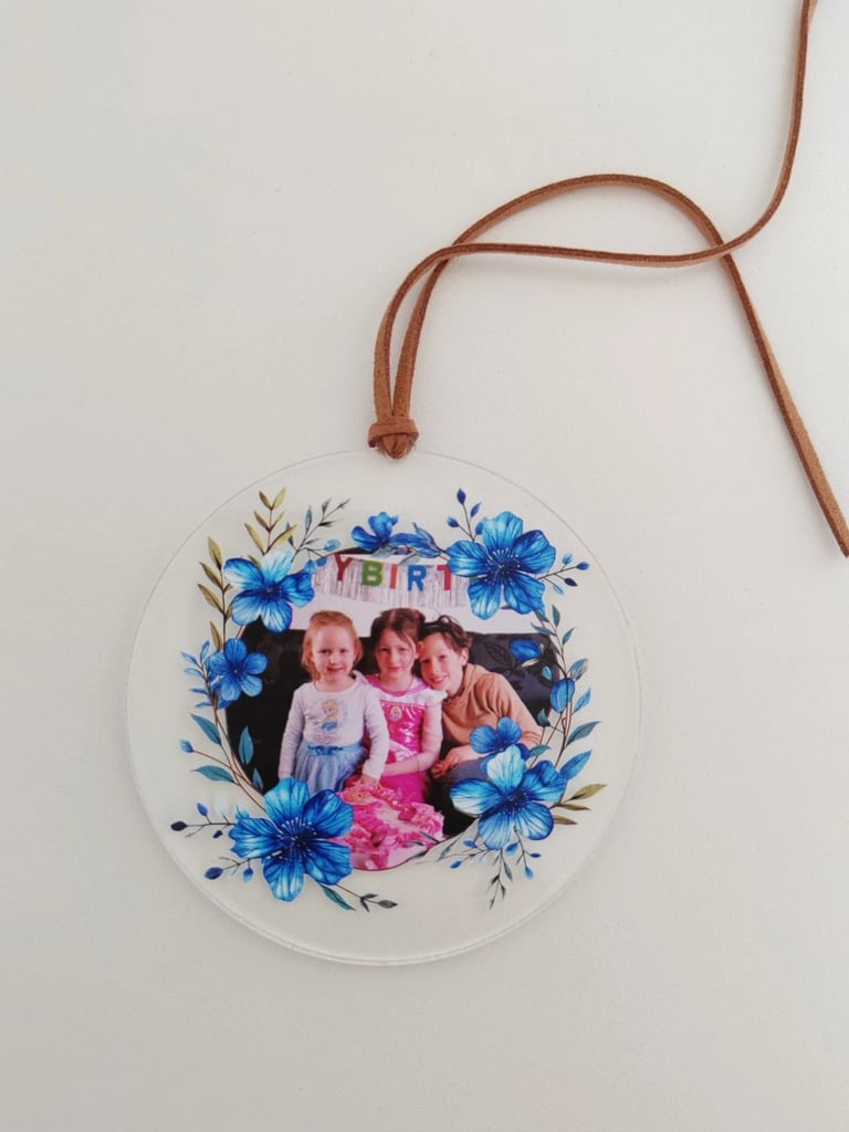 Customized round photo ornament featuring three children framed by blue floral illustrations and a suede hanging cord.