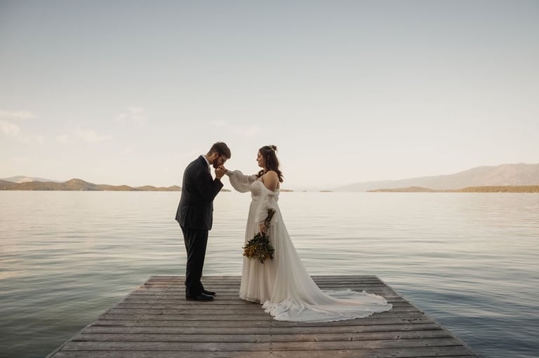 bride and groom portrait, dock on Flathead Lake, sunset, groom kisses bride's hand