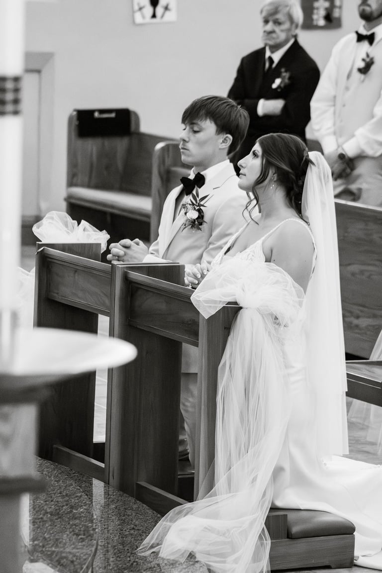 black and white photo of bride and groom kneeling during Catholic wedding ceremony