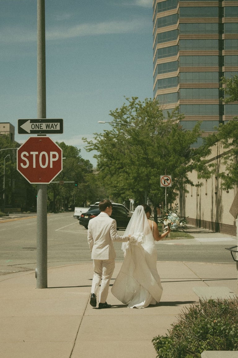 candid shot of groom holding bride's train, walking downtown