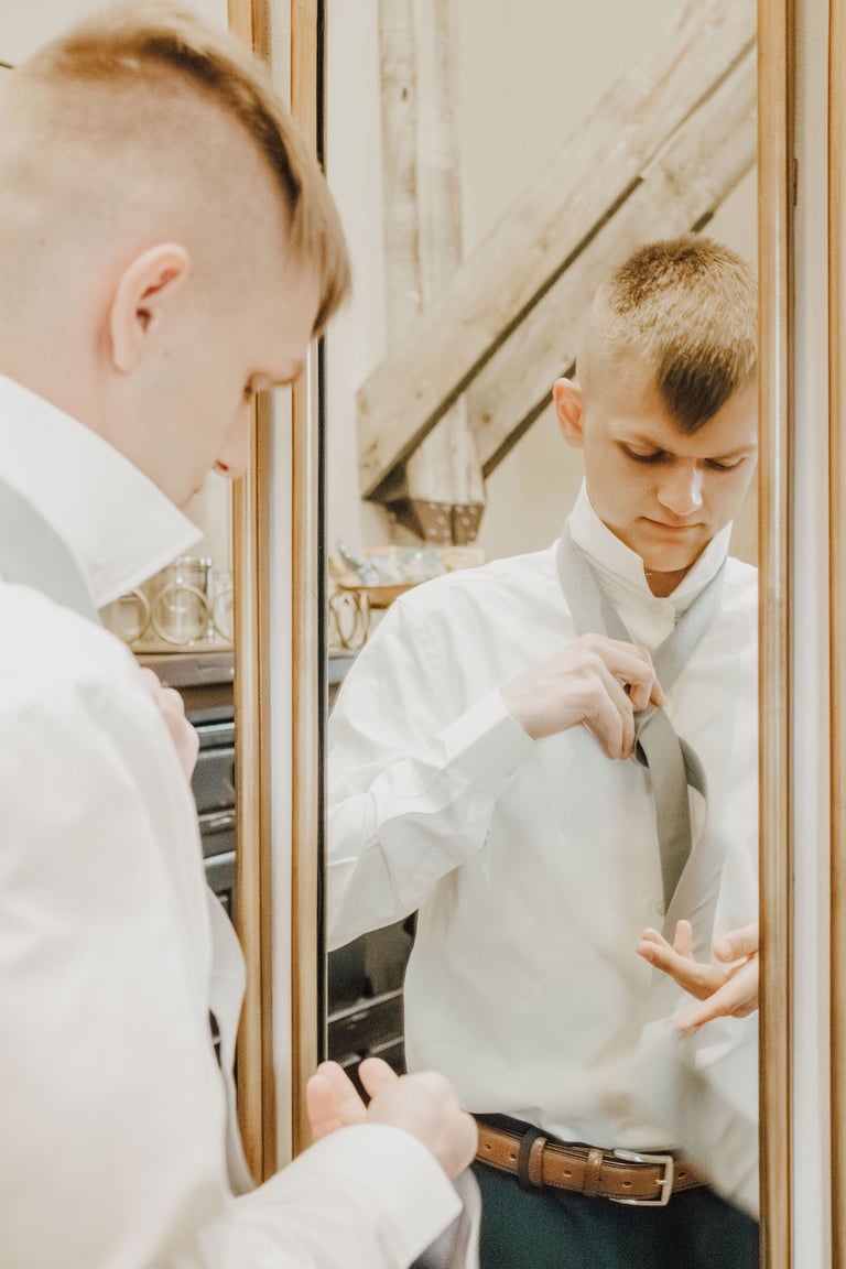 groom putting on tie in the mirror