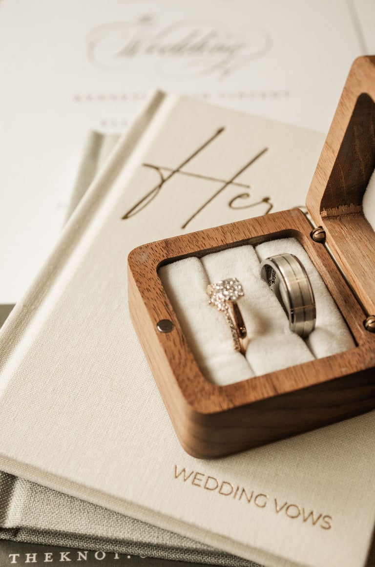 detail shot of wedding bands in a wooden box on stack of his and her vow books