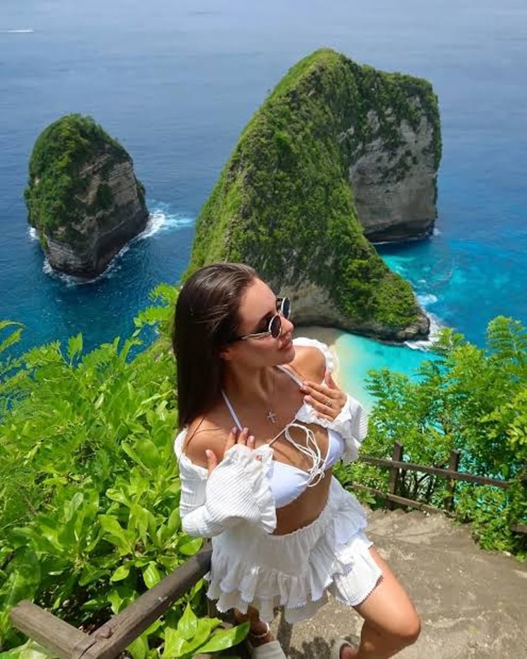 A woman in a white bikini overlooks Kelingking Beach's T-Rex cliff and turquoise water in Nusa Penida, Bali.