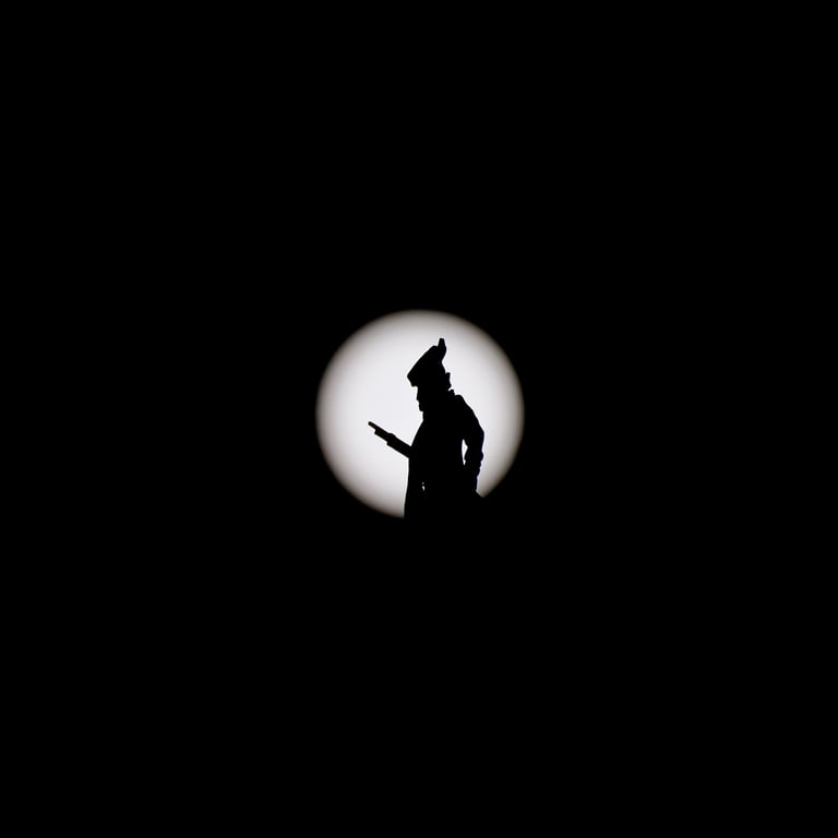 The silhouette of a Revolutionary War soldier weather vane against a solar-filtered sun.