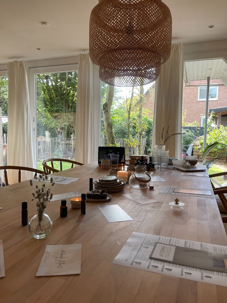 Essential oil workshop setup on a wooden dining table with candles and rattan pendant lighting.