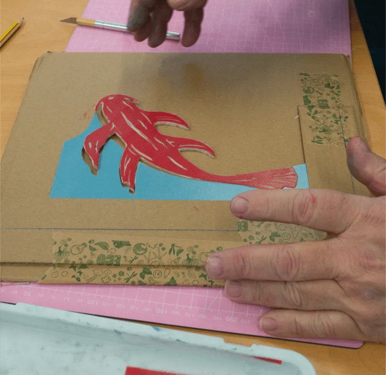 Person assembling pieces of cut lino together in a jigsaw print shaped like a fish