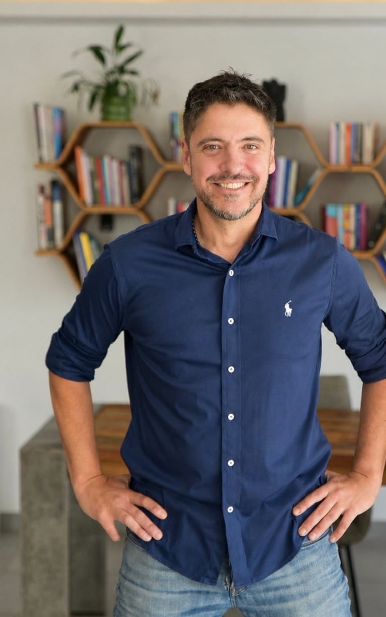 Smiling professional man in a blue button-down shirt standing in front of a modern bookshelf.