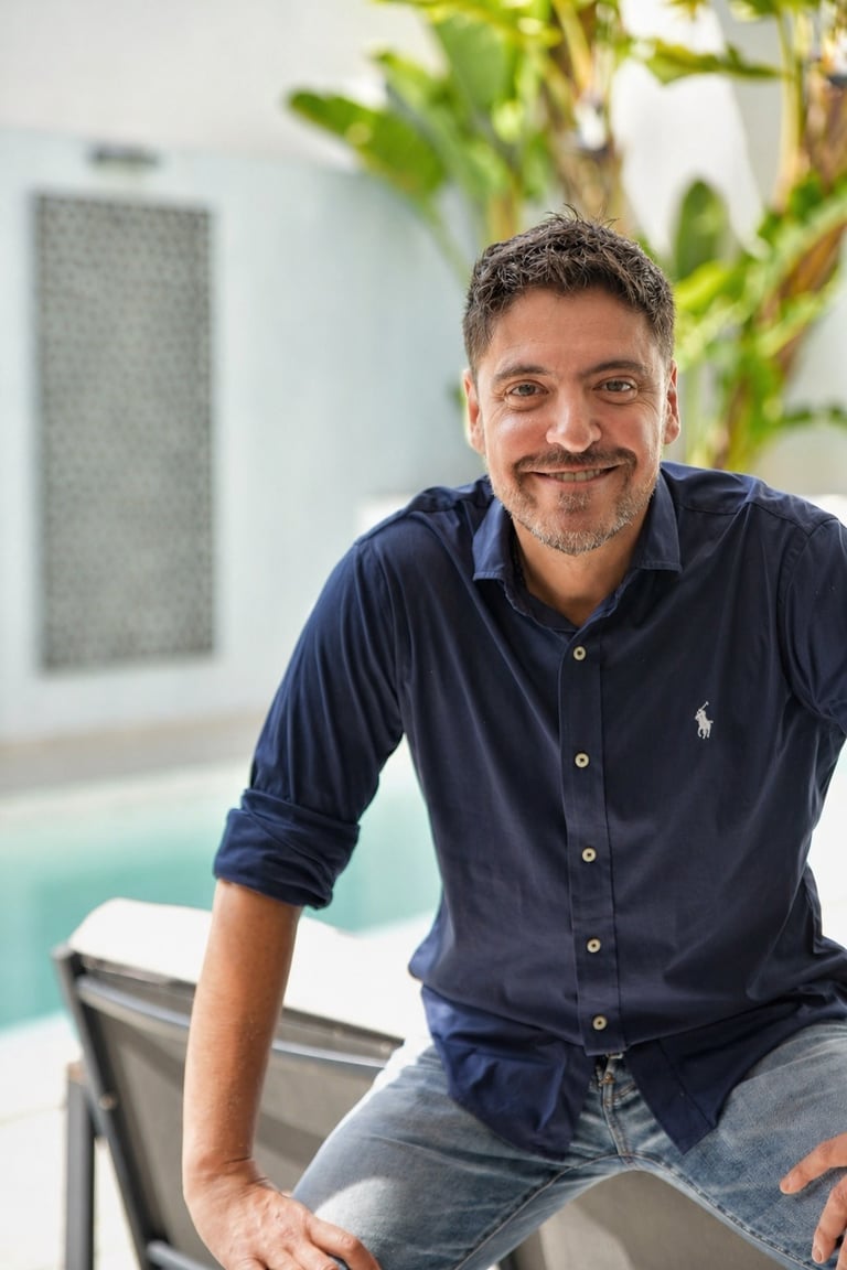 Smiling man in a navy blue Ralph Lauren polo shirt sitting outdoors by a swimming pool.
