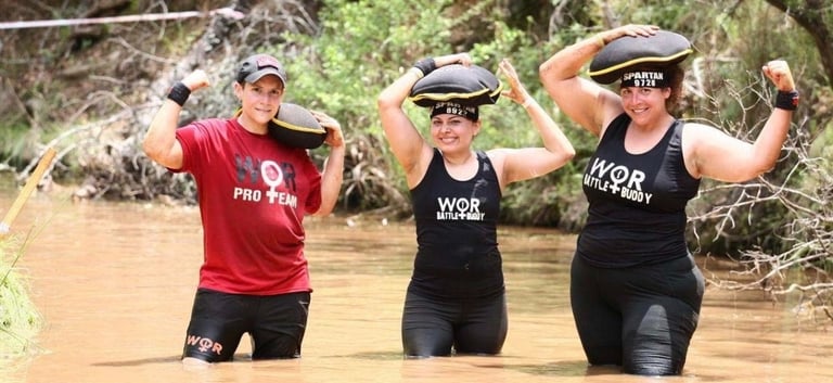 Women of Racing team members carrying sandbags through muddy water during a Spartan race.