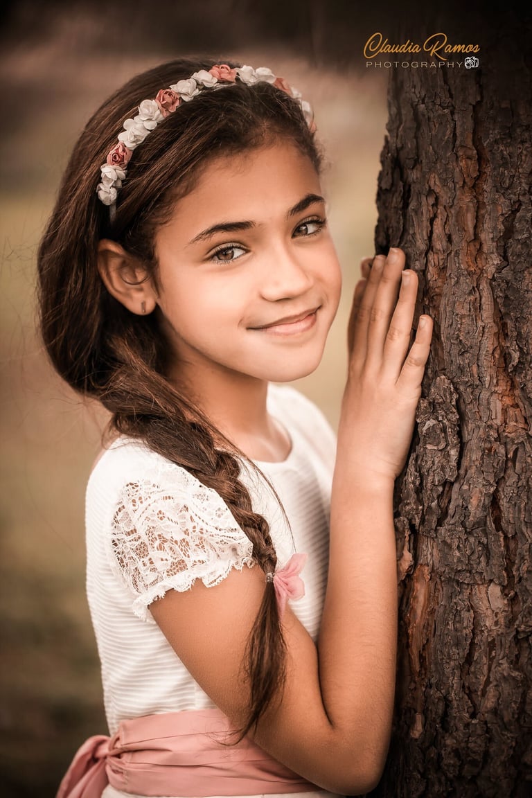 niña de comunión apoyada en un árbol