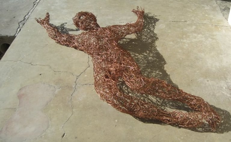 Copper wire scupture of Christ on the cross laying on  a concret surface