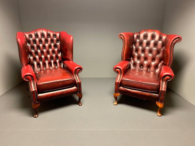Two vintage, orang leather armchairs with tufted backs sit side by side in a minimalist, neutral-colored room. 