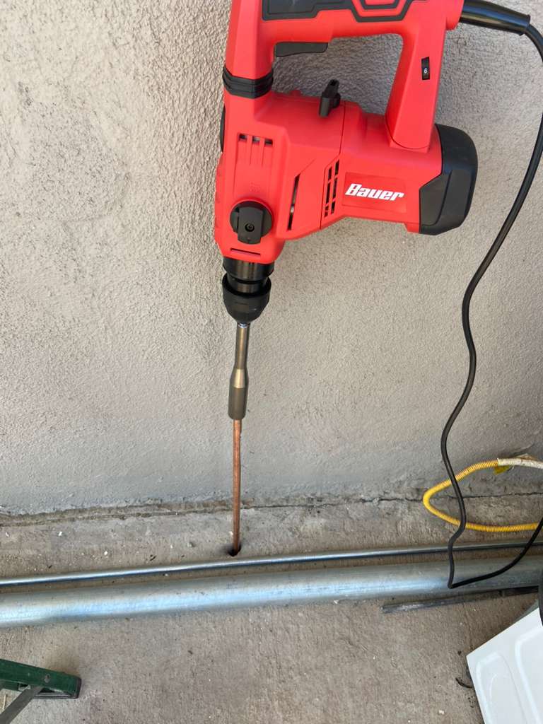 Red Bauer electric rotary hammer drill with chisel bit breaking into concrete surface