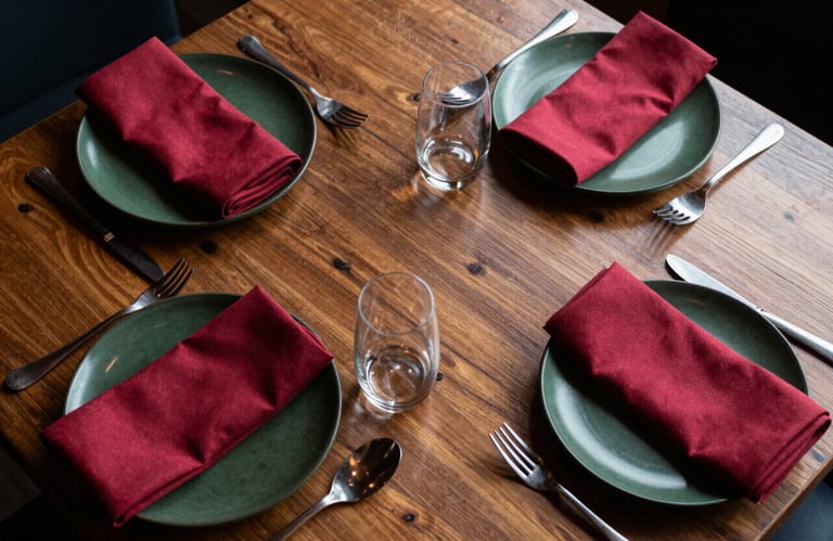 A top-down professional shot of an artisanal dining table in a North American restaurant, featuring dark forest green plates and crimson napkins.