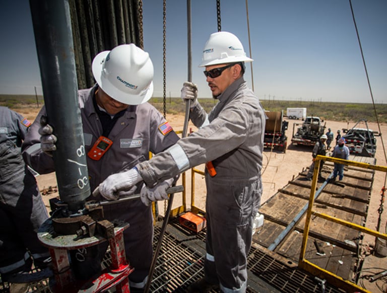 Oil and gas workers in safety gear operating heavy drilling equipment at an active oilfield site.