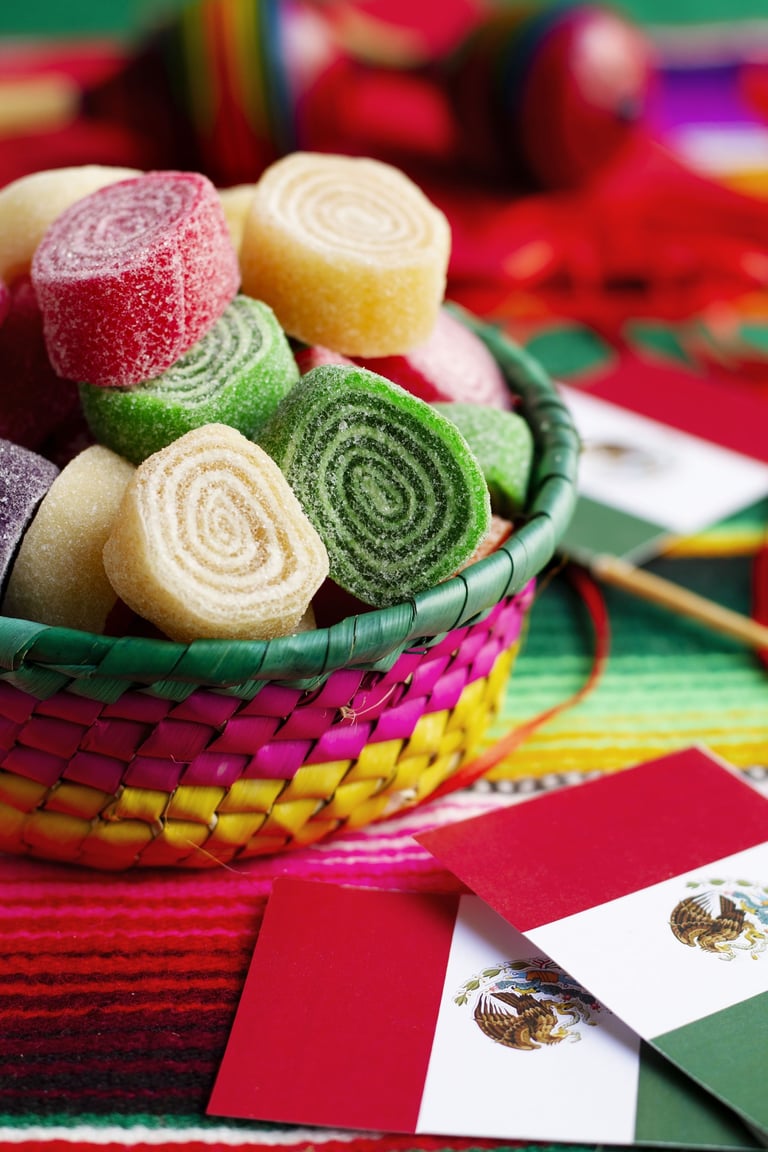 A colorful basket of Mexican fruit roll candies next to Mexico flags and a traditional zarape.