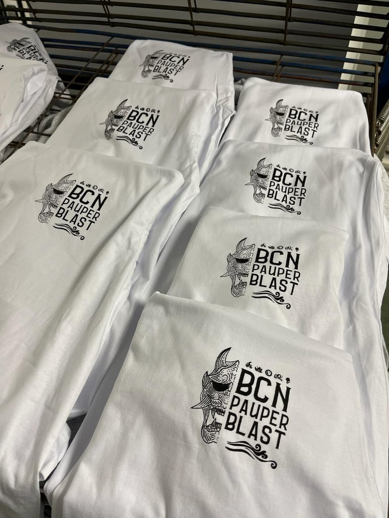 Stacked white BCN Pauper Blast custom t-shirts with black screen-printed graphic logos on a drying rack.