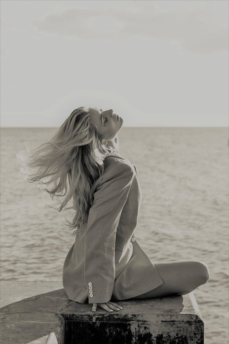 Orlane in an oversized blazer posing by sea with windblown hair in a black and white fashion shot.