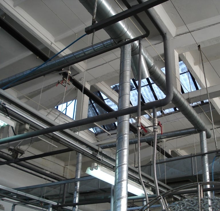 Industrial ceiling with metal HVAC ductwork and silver pipes in a warehouse facility.