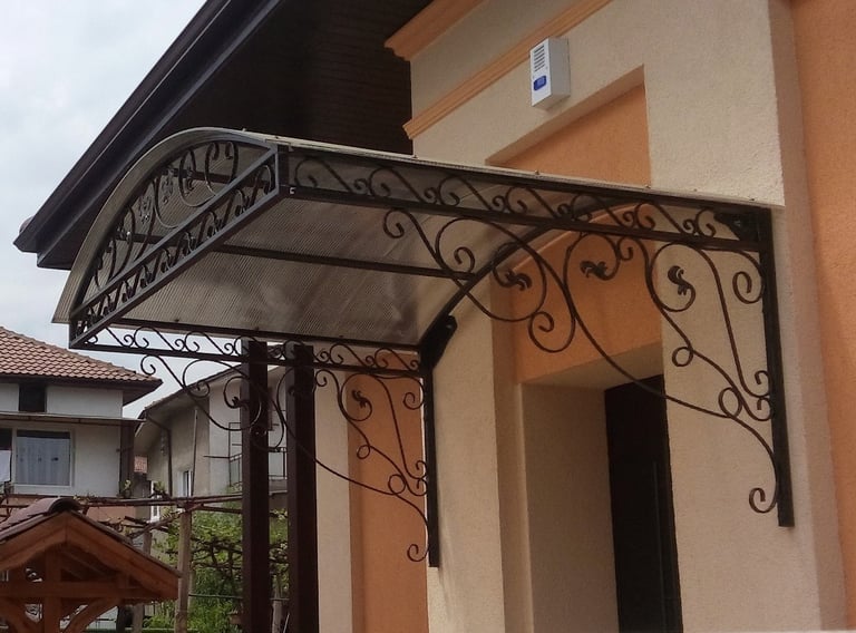 A decorative wrought iron door canopy with a curved polycarbonate roof installed over a house entrance.