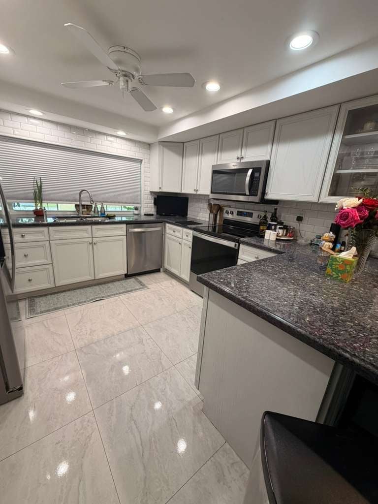 Modern kitchen with white shaker cabinets, dark granite countertops, and marble tile flooring.
