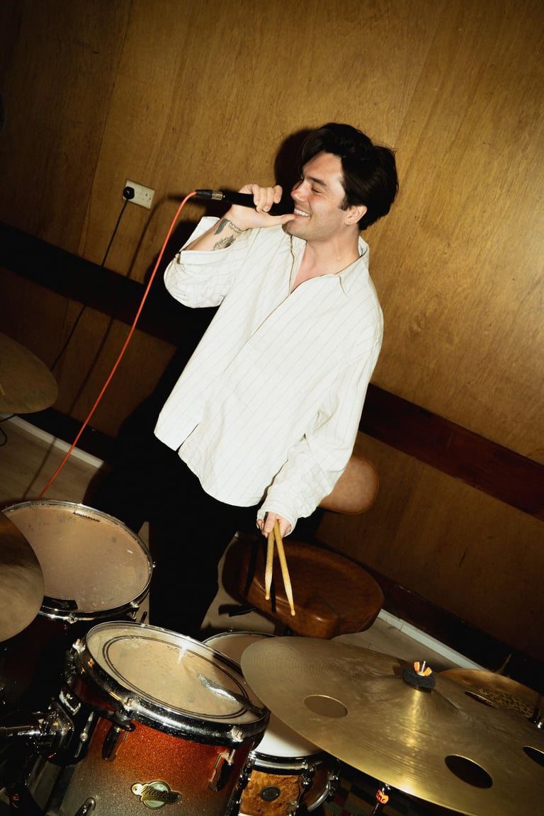 George Shelley singing in front of a drum kit