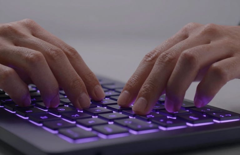 A close-up of a person's hands using a high-tech keyboard with deep purple backlit keys in a sleek, minimalist environment. Global / English-speaking.