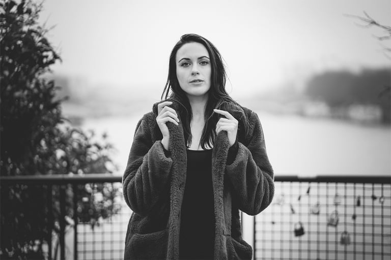 Portrait noir et blanc d’une femme en manteau, debout face caméra, au bord de la Seine, ambiance hivernale.