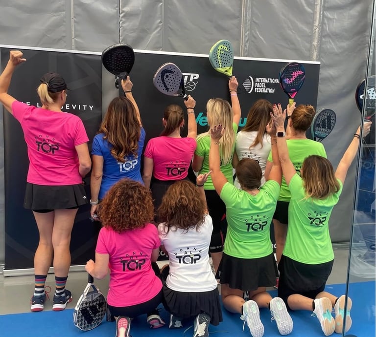A group of female padel players in colorful jerseys posing with rackets at an indoor court tournament.