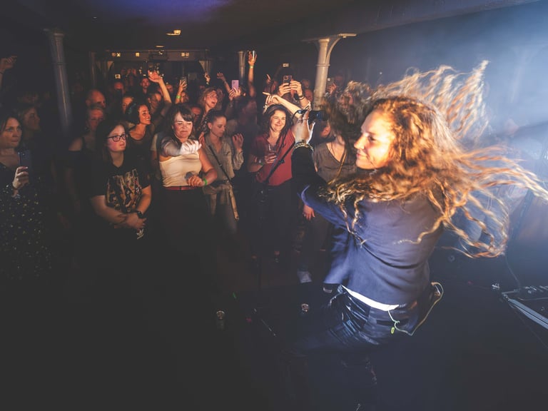 a singers hair flailing whilst performing to a crowd in a dark venue