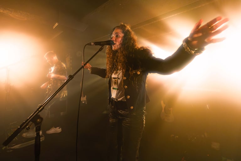 a dramatic image of a singer performing and hoding their arms wide with bright stagelights come from behind