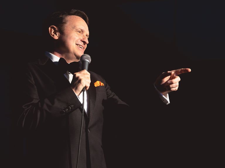 a singer in a suit and bow tie pointing to the crowd