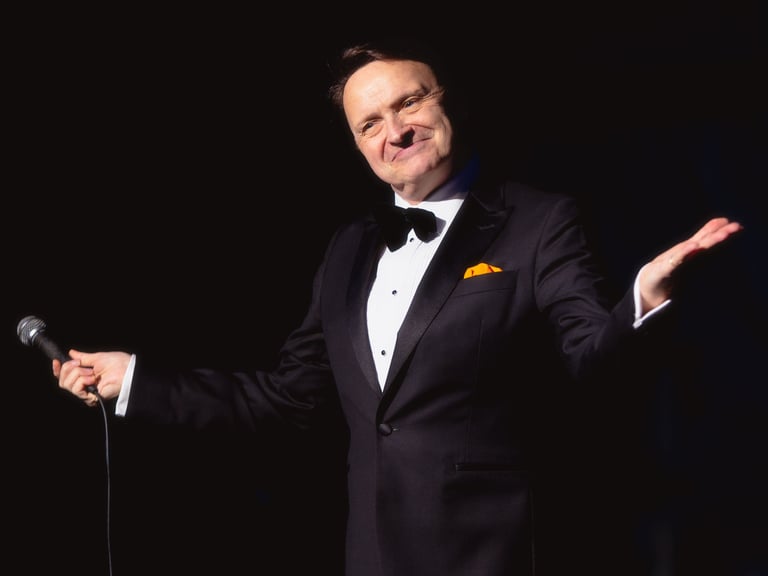 a singer in a suit and bow tie holding their arms out to the crowd and smiling