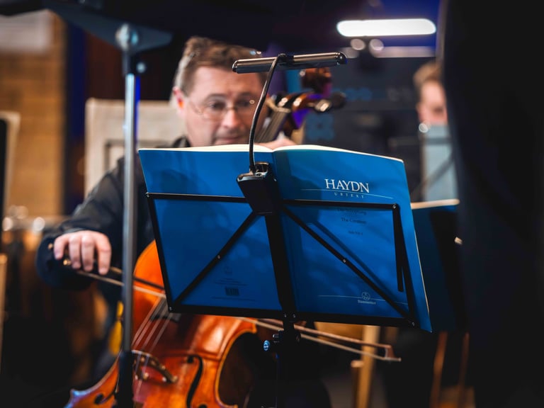 A photo of a music book on a stand with the performing cellist in the background