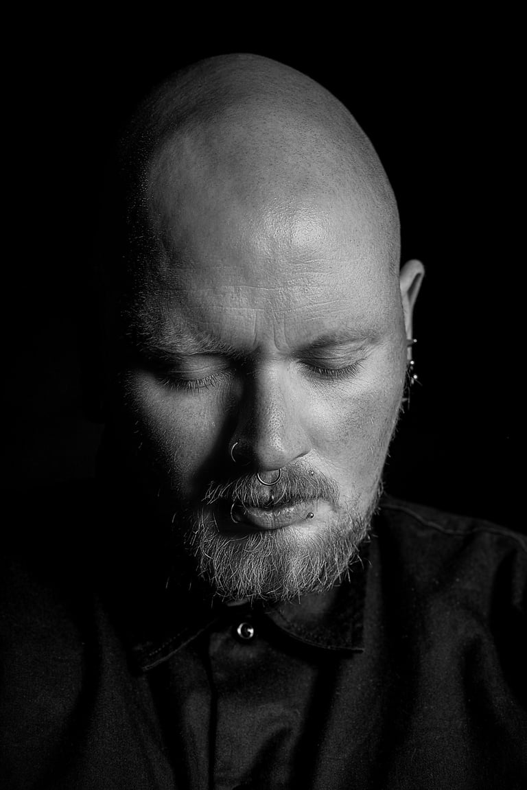 Schwarzweiß-Portrait eines Mannes mit Bart vor dunklem Hintergrund