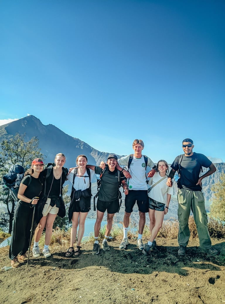 A group of happy hikers with backpacks standing at Senaru Crater overlooking a scenic volcano lake.
