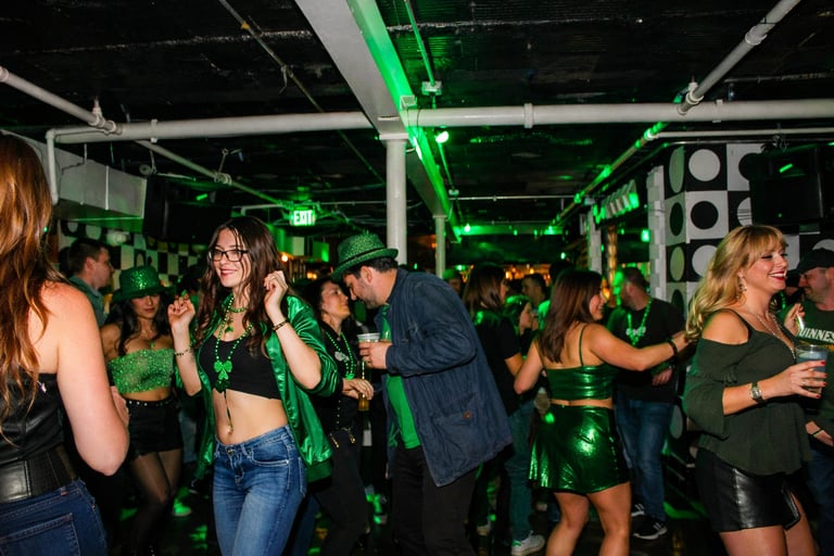 A young diverse crowd celebrates St. Patrick's Day dancing in green at an industrial nightclub.