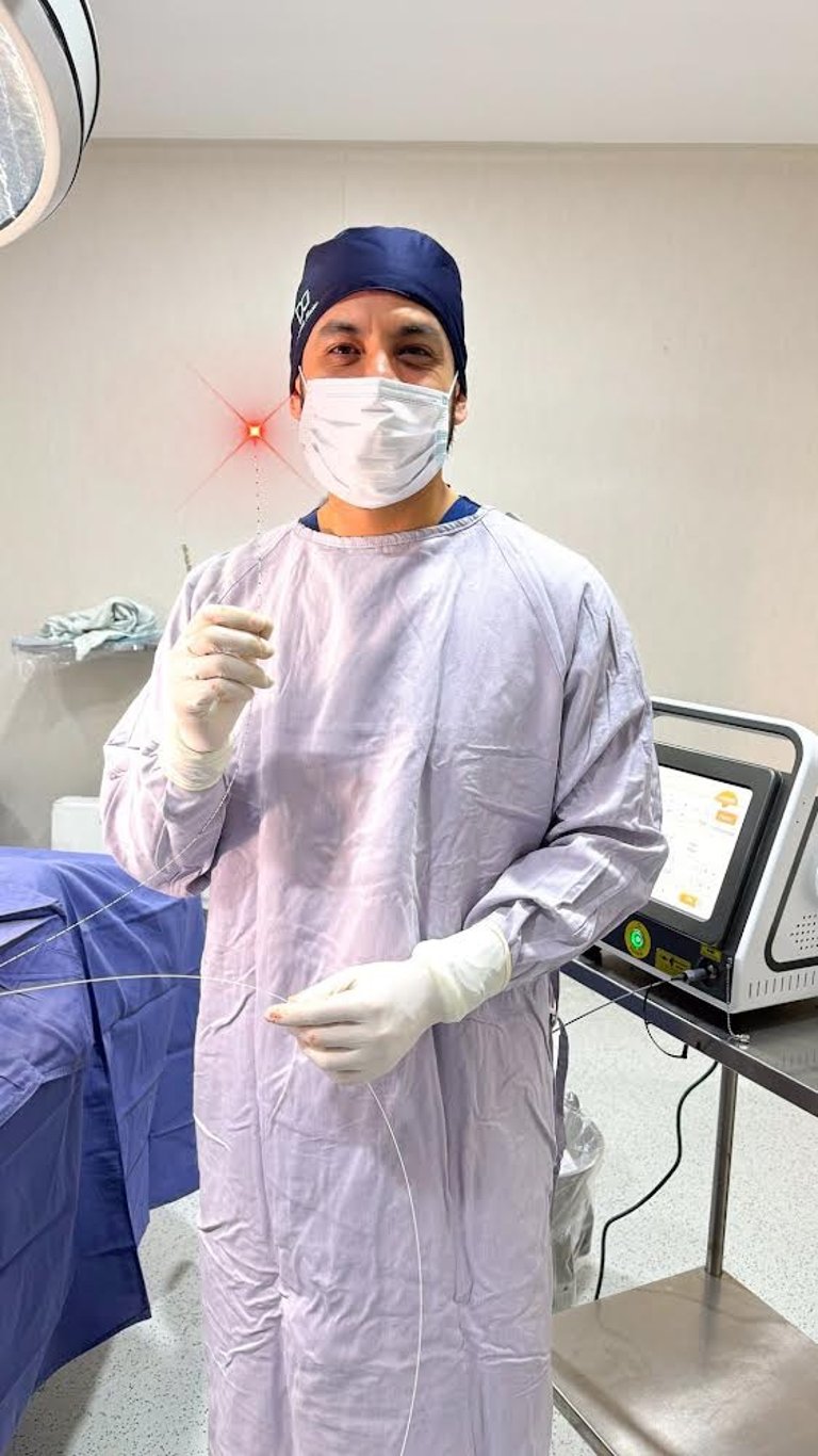 Surgeon in sterile scrubs holding a medical laser fiber during a surgical procedure in an operating room.