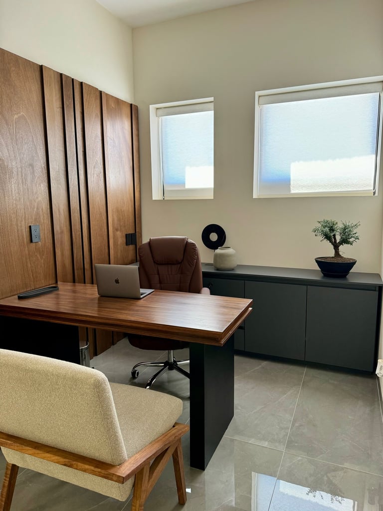 Modern home office with a wooden desk, leather chair, laptop, and bonsai tree.