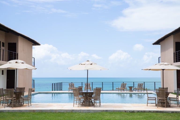 Luxury beachfront resort pool with patio furniture and umbrellas overlooking the blue ocean.