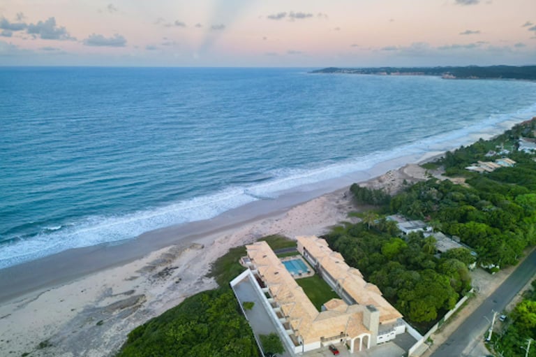 Aerial view of a luxury beachfront resort and swimming pool on a tropical sandy beach with ocean waves.