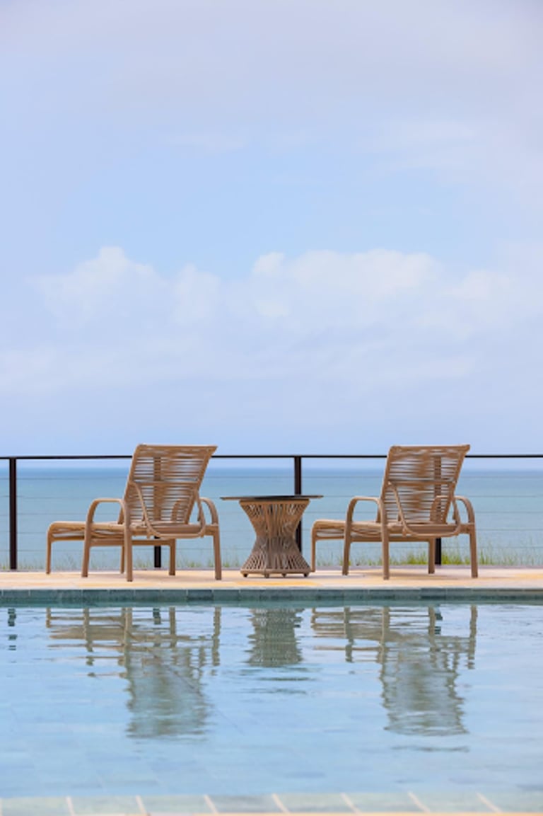 Modern wicker patio lounge chairs and side table on a luxury poolside deck with ocean views.