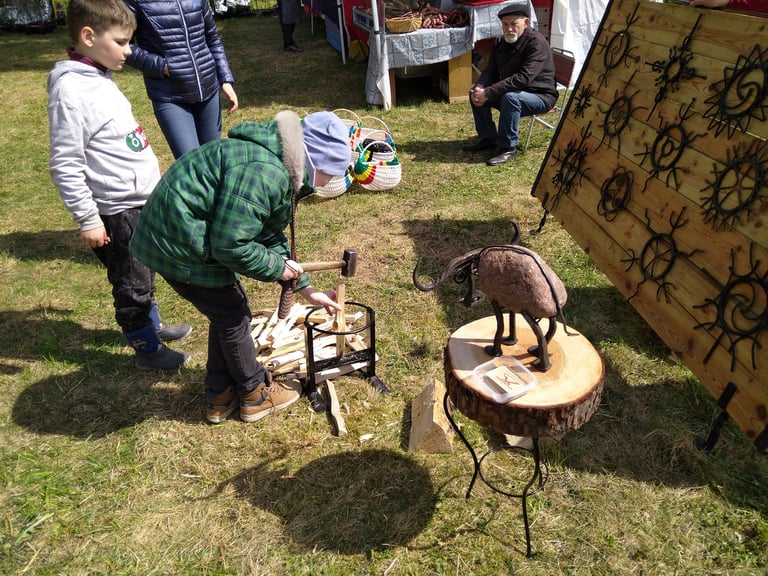Edukacinio užsiėmimo metu vaikai saugiai moko skaldyti malkas laužui, naudodami rankų darbo kalvišką skaldyklę