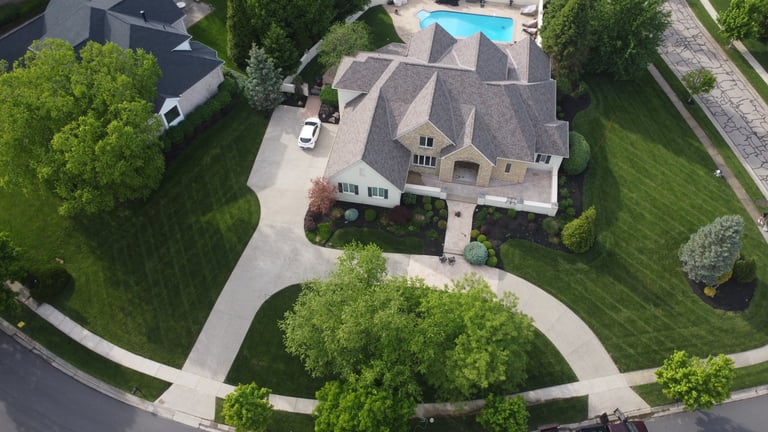 Aerial view of a luxury suburban home with a manicured green lawn, driveway, and backyard swimming pool.