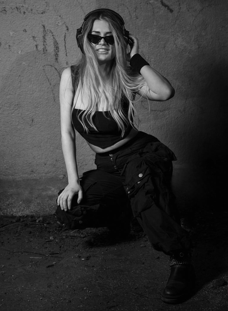 Dj Kat in black streetwear and sunglasses wearing headphones in a black and white urban portrait.